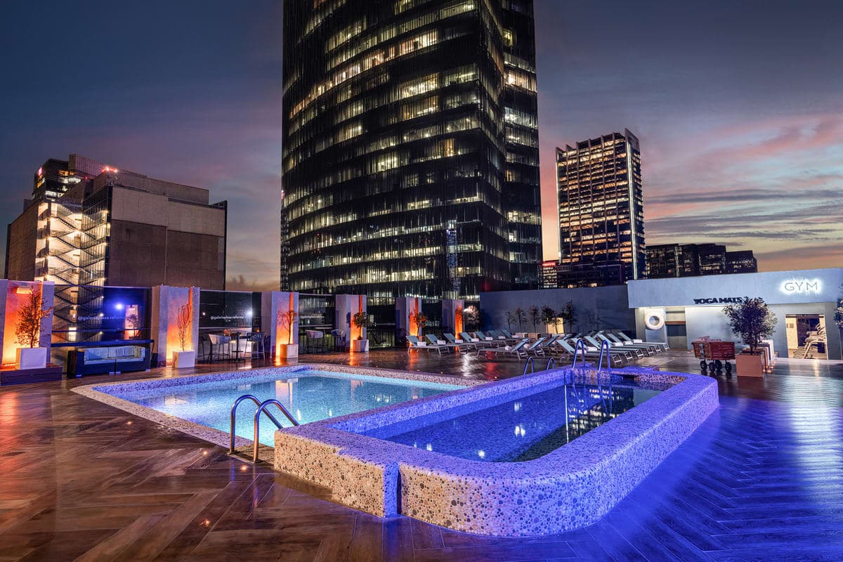 The rooftop pool and terrace at Galería Plaza Reforma at dusk, with the Mexico City skyline behind